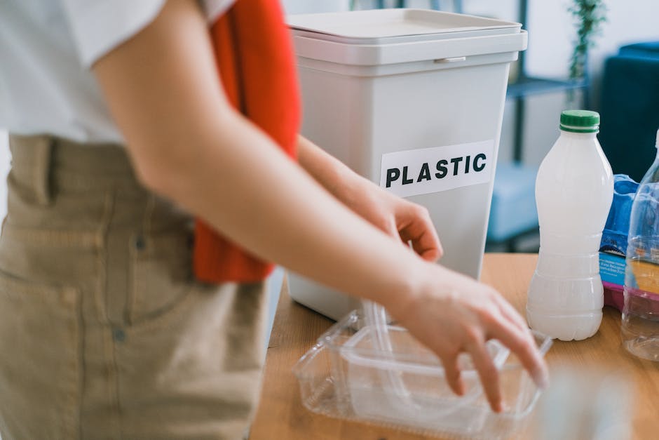 A person wearing a white shirt and beige pants, with an orange sleeveless cardigan, is seen holding a crumpled brown paper bag over a table cluttered with more crumpled paper bags and plastic waste. I